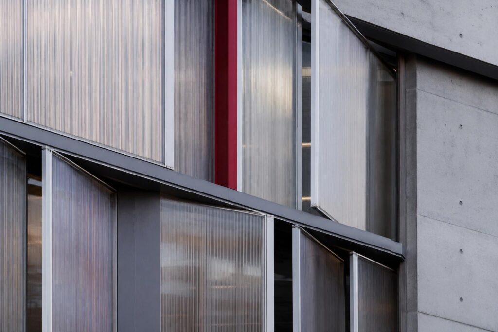 Close-up of decorative translucent polycarbonate facade panels with ribbed texture, metal framing, concrete details, and a red accent panel