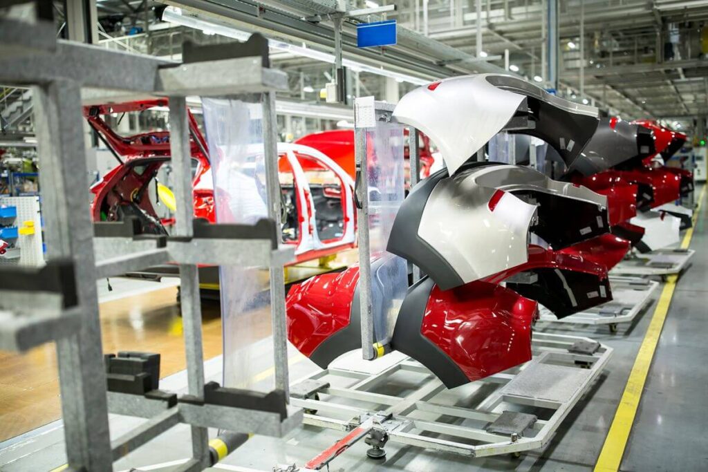 Automotive manufacturing line with painted vehicle body panels and car frames being assembled inside a modern factory