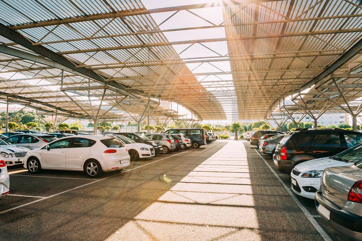Outdoor parking area covered by transparent polycarbonate roofing that allows natural light to reach the vehicles below