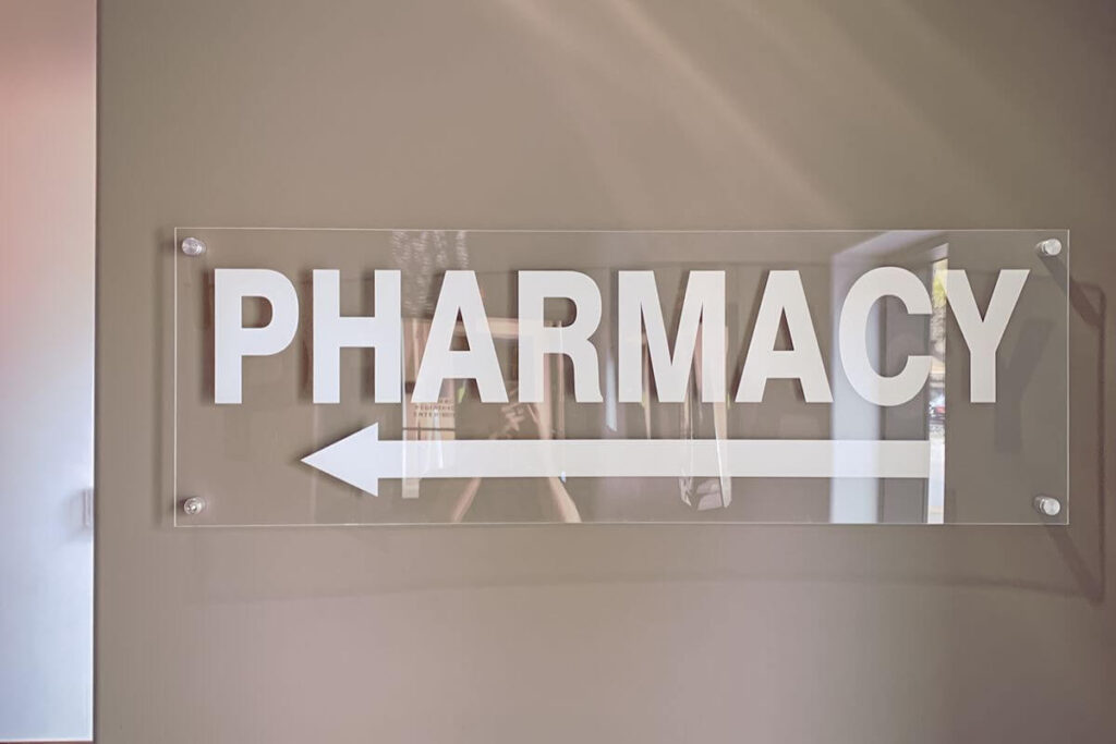 Clear acrylic pharmacy direction sign with white lettering and a left-pointing arrow mounted on a wall