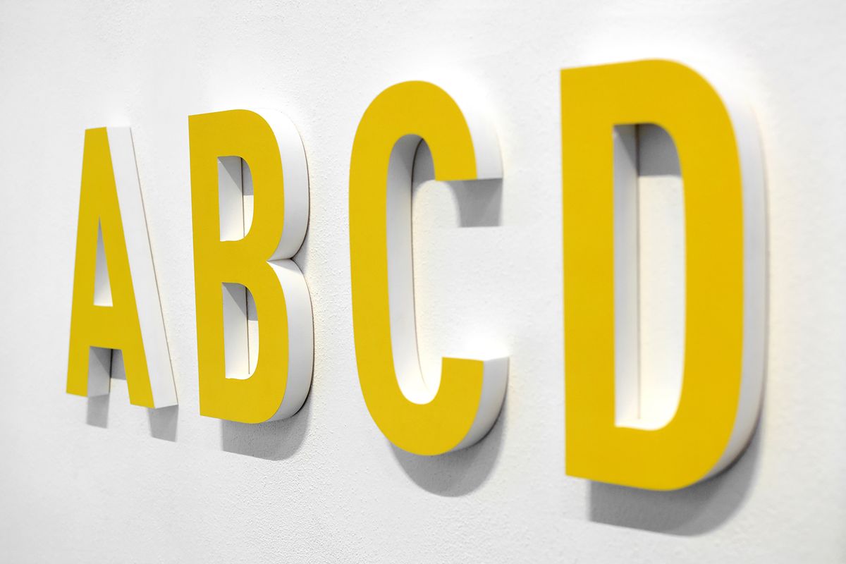 Close-up of yellow and white dimensional acrylic letters mounted on a white wall for commercial signage