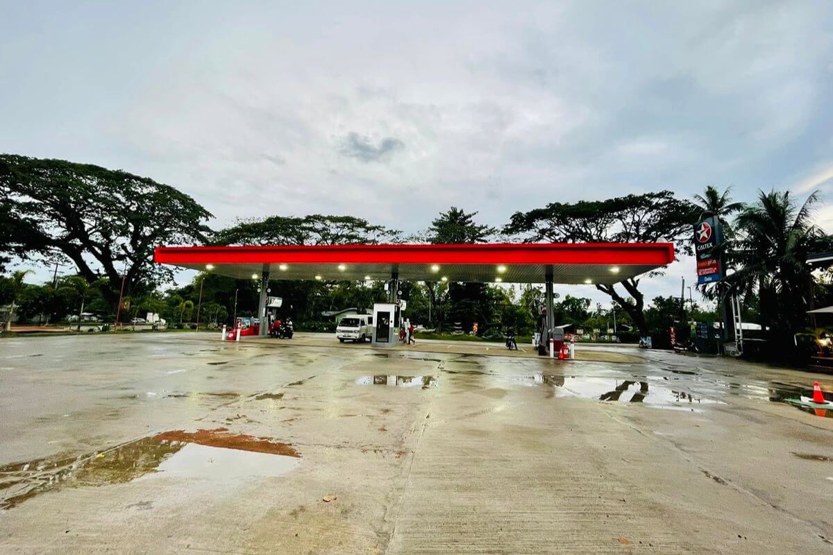 Fuel station canopy finished with red architectural panels above the pumps on a cloudy day
